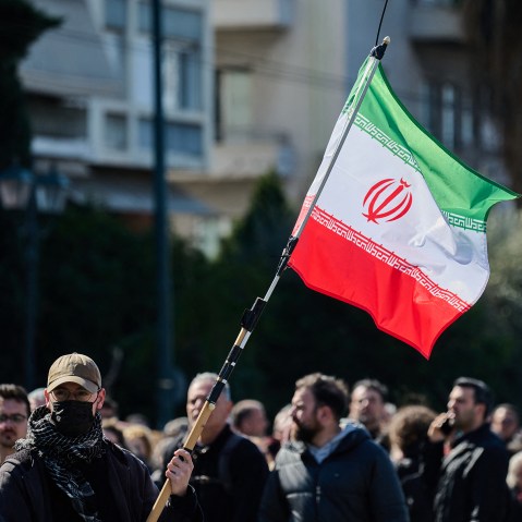 A man waves an Iranian flag in front of a crowd during a protest.