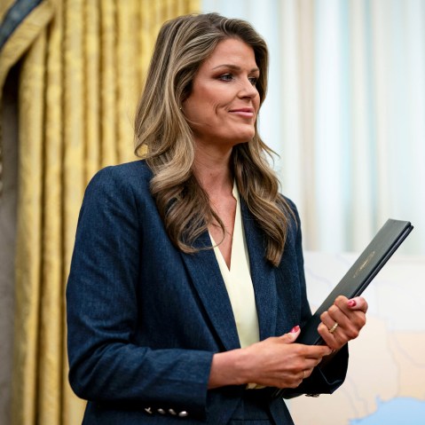 Lindsey Halligan smiles while holding proclamations in her hands in the Oval Office.