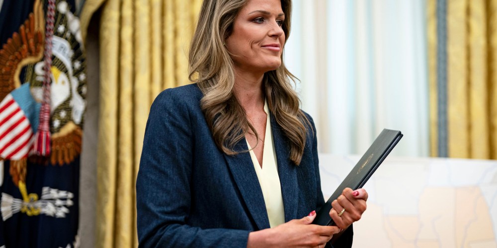 Lindsey Halligan smiles while holding proclamations in her hands in the Oval Office.