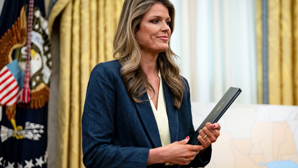 Lindsey Halligan smiles while holding proclamations in her hands in the Oval Office.