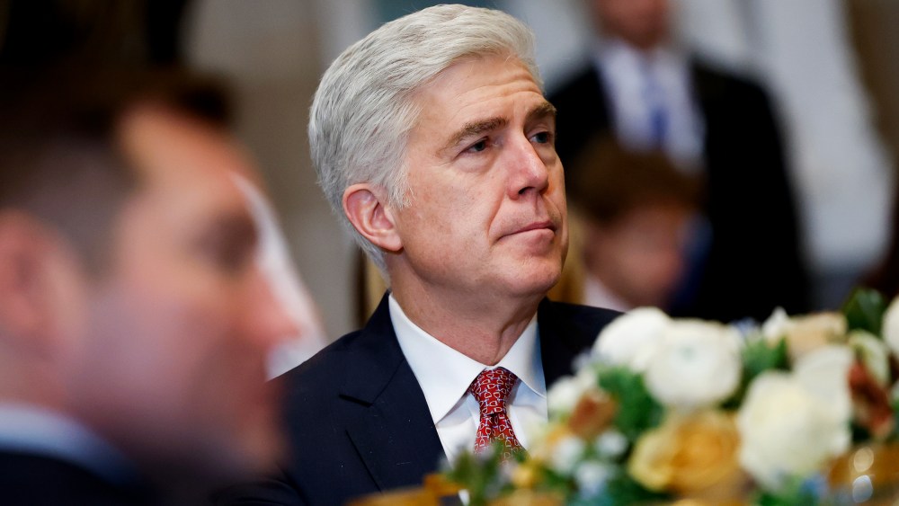 Neil Gorsuch looks on as he sits at a table with other people.