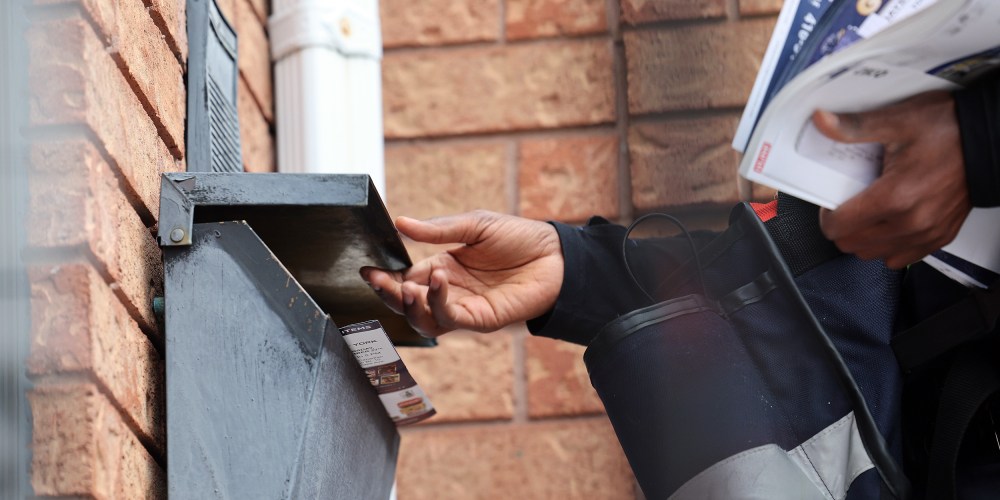A Post carrier works handing out flyers with mail on his route.