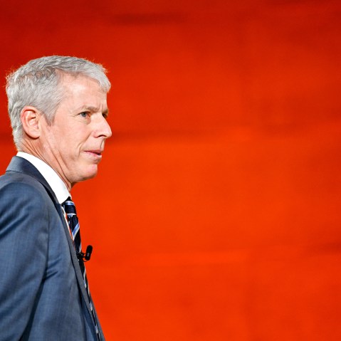 Chris Wrights walks towards right side of the frame in front of a red background.