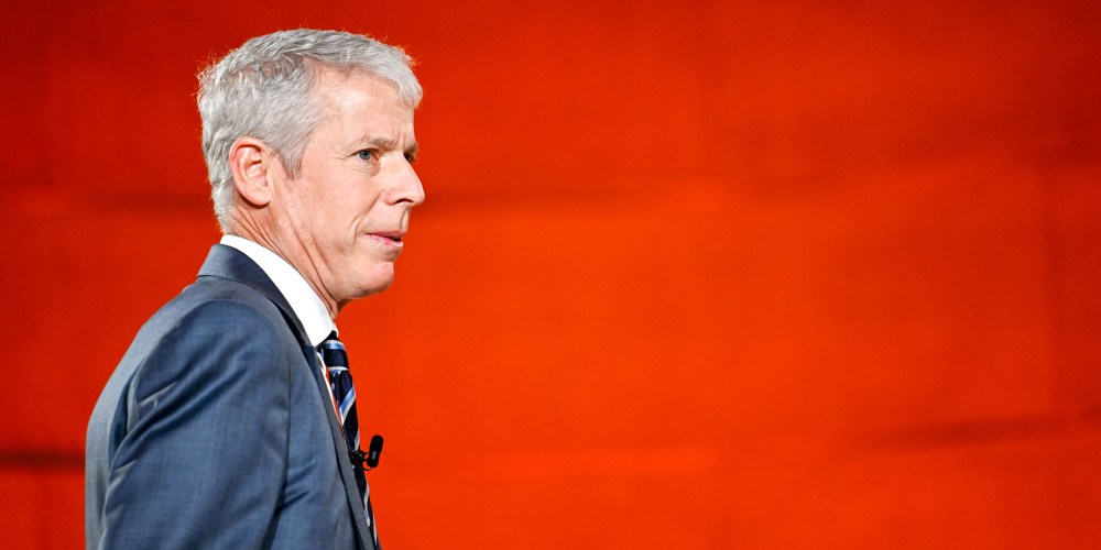 Chris Wrights walks towards right side of the frame in front of a red background.