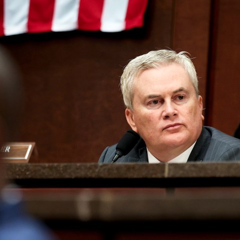 James Comer sits behind other members of the congress in front of an American flag.