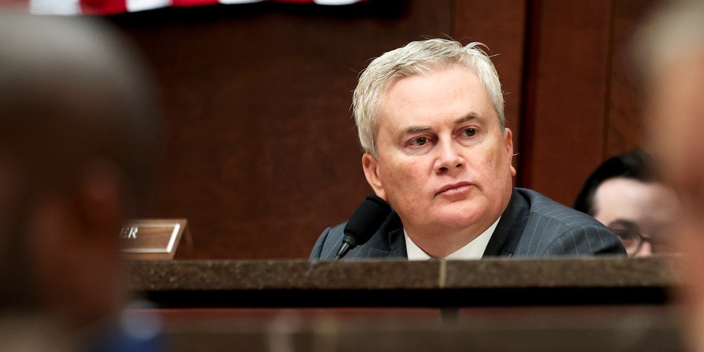 James Comer sits behind other members of the congress in front of an American flag.