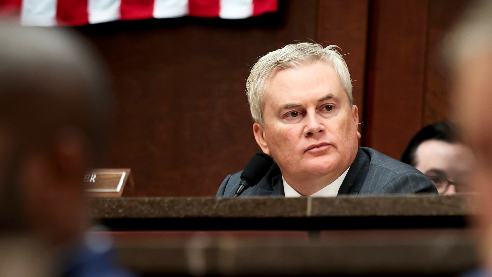 James Comer sits behind other members of the congress in front of an American flag.