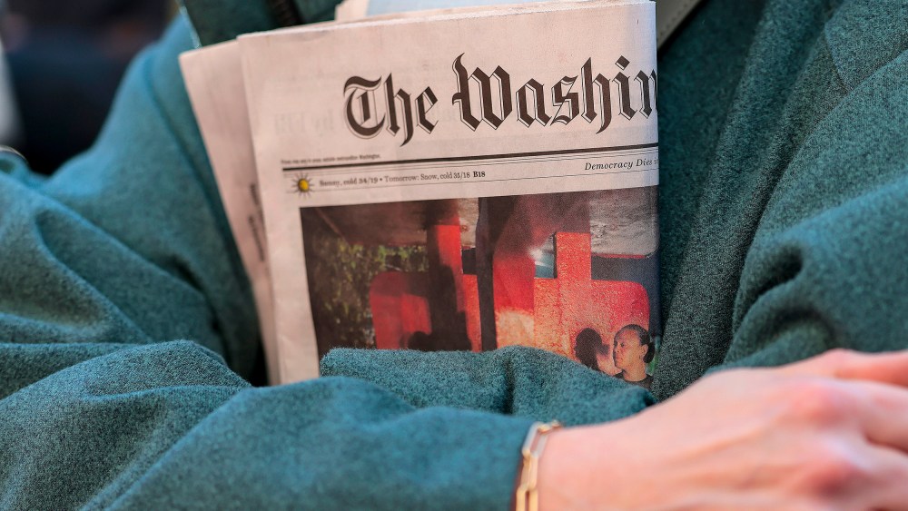 In this close-up shot of crossed arms, a woman holds a copy of The Washington Post tightly.