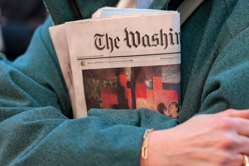 In this close-up shot of crossed arms, a woman holds a copy of The Washington Post tightly.