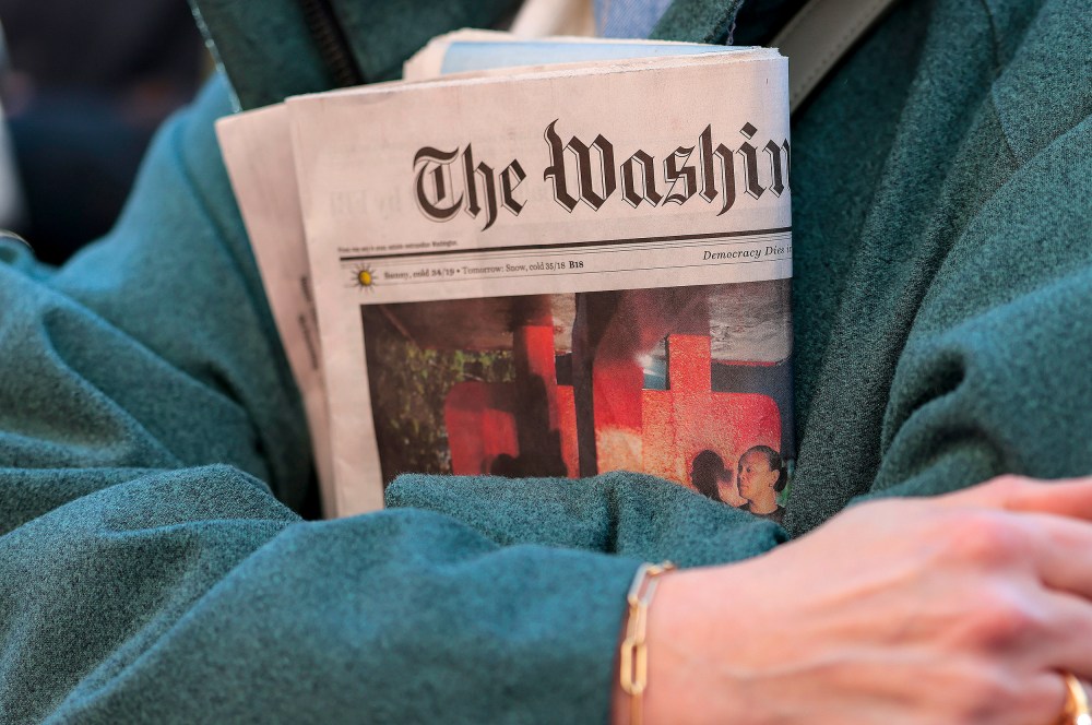In this close-up shot of crossed arms, a woman holds a copy of The Washington Post tightly.